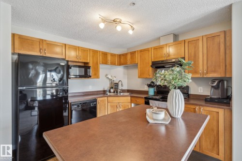 Kitchen with wood-finish cabinetry, black appliances, a track lighting fixture, and a center island with countertop seating - 1306 330 Clareview Station Drive, Edmonton, AB - Indoor Photo Showing Kitchen With Double Sink