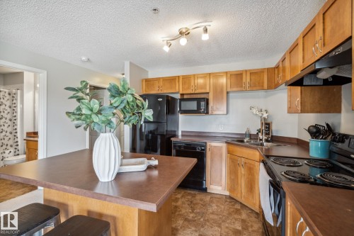 Kitchen featuring wood cabinetry, black appliances, track lighting, and a peninsula with countertop seating - 1306 330 Clareview Station Drive, Edmonton, AB - Indoor Photo Showing Kitchen