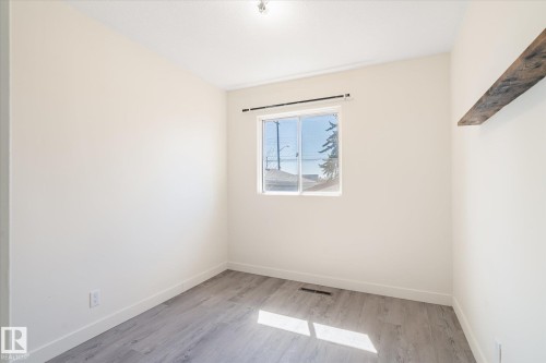 Bright room featuring light-toned walls, wood-finish flooring, a window with a dark curtain rod, and a single floating wood shelf - 10531 128 Avenue, Edmonton, AB - Indoor Photo Showing Other Room