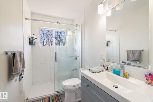 Modern bathroom featuring a glass-enclosed shower with white subway tile, a window, a single vanity with a white countertop, and an integrated sink with a chrome faucet - 10531 128 Avenue, Edmonton, AB - Indoor Photo Showing Bathroom