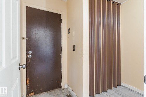 Entryway featuring a dark paneled door with a deadbolt, a light-colored interior door, a bi-fold closure, and light-toned floor tiling - 10531 128 Avenue, Edmonton, AB - Indoor Photo Showing Other Room