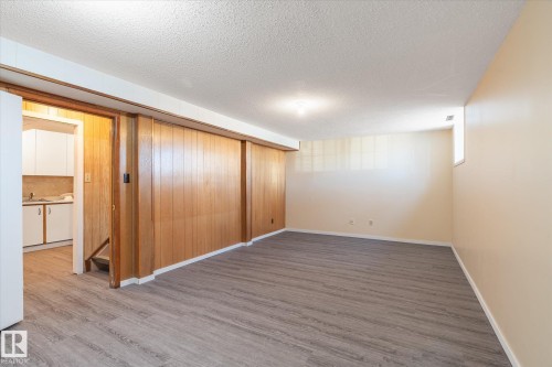 Spacious lower-level room featuring wood-finish paneling, light-toned walls, and wood-finish flooring - 10531 128 Avenue, Edmonton, AB - Indoor Photo Showing Other Room