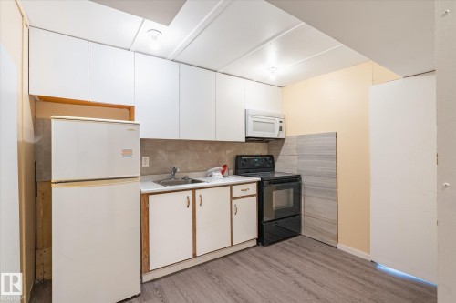 Kitchen featuring white upper cabinetry, a stainless steel sink, wood-finish flooring, a built-in microwave, and an electric range - 10531 128 Avenue, Edmonton, AB - Indoor Photo Showing Kitchen