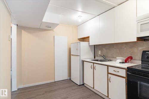 Kitchen area featuring white cabinetry, a double-door refrigerator, and a black electric range - 10531 128 Avenue, Edmonton, AB - Indoor Photo Showing Kitchen