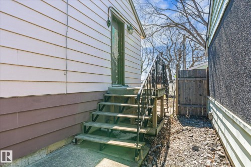 Exterior entry with a wood staircase, black metal railing, and white horizontal siding - 10531 128 Avenue, Edmonton, AB - Outdoor With Exterior
