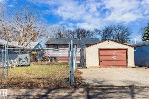 Detached garage with a brown door and textured stucco exterior, accompanied by a chain-link fence and a grassy yard - 10531 128 Avenue, Edmonton, AB - Outdoor
