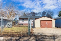 Detached garage with a brown door and textured stucco exterior, accompanied by a chain-link fence and a grassy yard - 