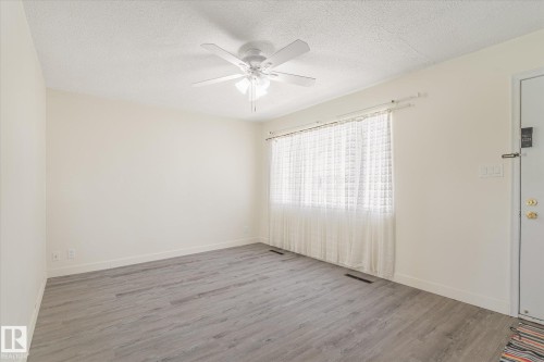Open concept living space featuring wood-finish flooring, a ceiling fan with integrated lighting, and a large window with privacy coverings - 10531 128 Avenue, Edmonton, AB - Indoor Photo Showing Other Room