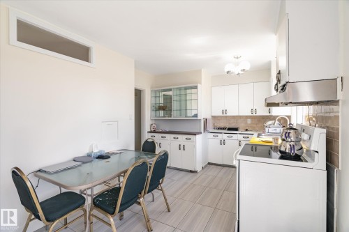 Kitchen featuring white cabinetry, tile backsplash, stainless steel range hood, and tile flooring - 10531 128 Avenue, Edmonton, AB - Indoor