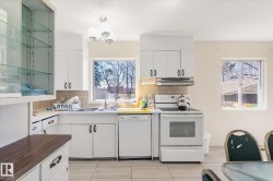 Well-lit kitchen featuring white cabinetry, a built-in dishwasher, white electric range, and a dual-basin sink with a window overhead - 
