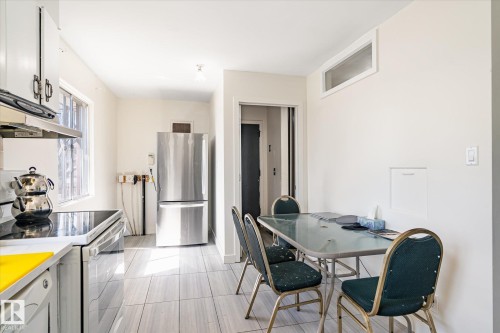 Kitchen featuring white cabinetry with dark hardware, a stainless steel refrigerator, and a built-in range with an overhead vent - 10531 128 Avenue, Edmonton, AB - Indoor