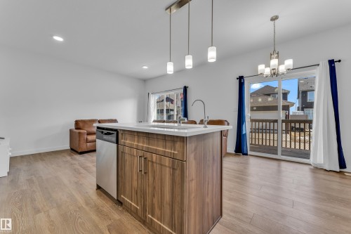 Central kitchen island with wood-finish cabinetry, white countertop, and integrated stainless steel dishwasher - 41 603 Orchards Boulevard, Edmonton, AB - Indoor Photo Showing Kitchen