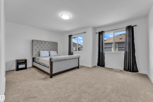 Spacious bedroom featuring light-colored carpeting, white walls, and a contemporary flush-mount ceiling light - 41 603 Orchards Boulevard, Edmonton, AB - Indoor