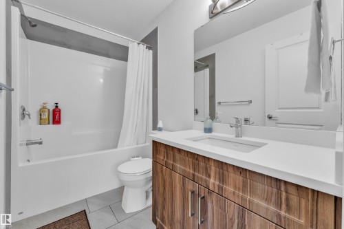 Modern bathroom featuring a wood-finish vanity with an integrated sink and chrome faucet, a large frameless mirror, and a full-size bathtub with a shower - 41 603 Orchards Boulevard, Edmonton, AB - Indoor Photo Showing Bathroom