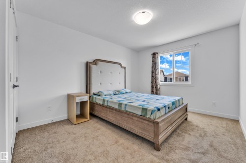 Bright bedroom featuring neutral carpeting, white walls, and a single window with curtain rods - 41 603 Orchards Boulevard, Edmonton, AB - Indoor Photo Showing Bedroom