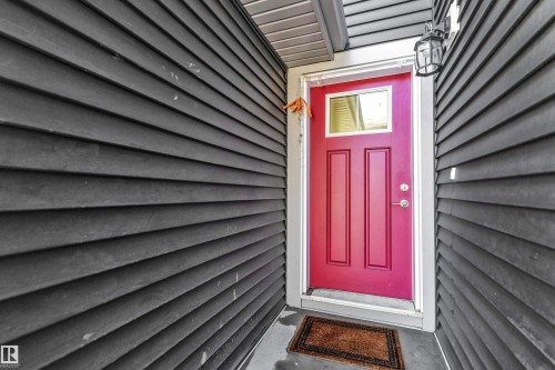 Entryway featuring a bright red paneled door with an upper window, framed by white trim and dark horizontal siding - 41 603 Orchards Boulevard, Edmonton, AB - Outdoor