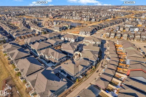 Aerial perspective showcasing a dense residential development with numerous single-family homes and townhomes, a central street network, and a prominent pond feature - 41 603 Orchards Boulevard, Edmonton, AB - Outdoor With View