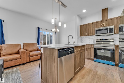 Kitchen island with light-toned countertop, stainless steel appliances, wood-finish cabinetry, subway tile backsplash, and light wood-finish flooring - 41 603 Orchards Boulevard, Edmonton, AB - Indoor Photo Showing Kitchen