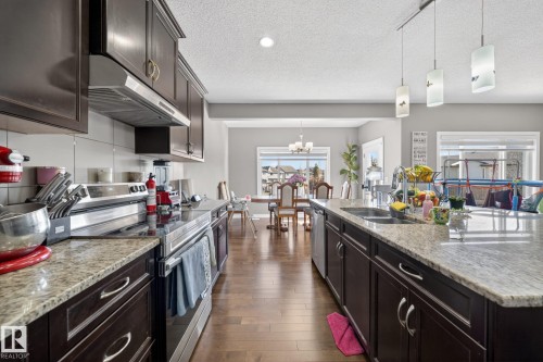 Open-concept kitchen featuring dark wood cabinetry, granite countertops, a stainless steel electric range, and a large center island with an undermount double sink - 3639 15A Street, Edmonton, AB - Indoor Photo Showing Kitchen With Double Sink
