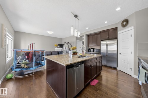 Open-concept kitchen featuring an island with a double basin sink, stainless steel dishwasher, dark wood cabinetry, and granite-finish countertops - 3639 15A Street, Edmonton, AB - Indoor Photo Showing Kitchen With Double Sink With Upgraded Kitchen