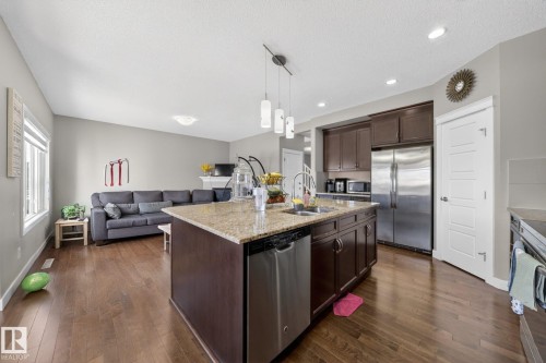 Open-concept kitchen and living area featuring wood-finish flooring, a kitchen island with granite countertop and undermount sink, stainless steel appliances, dark wood cabinetry, and recessed lighting - 3639 15A Street, Edmonton, AB - Indoor Photo Showing Kitchen With Double Sink With Upgraded Kitchen