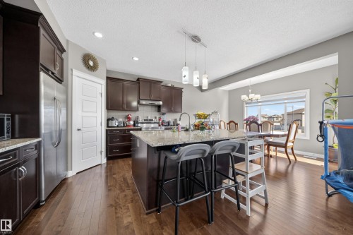 Spacious kitchen featuring an island with a light-toned countertop, dark wood-finish cabinetry, stainless steel appliances, and wood-finish flooring - 3639 15A Street, Edmonton, AB - Indoor Photo Showing Other Room
