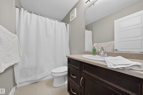 Bathroom featuring a dark wood-finish vanity with an integrated sink, a light-toned countertop, a large wall-mounted mirror, track lighting, and a bathtub with a shower and white shower curtain - 3639 15A Street, Edmonton, AB - Indoor Photo Showing Bathroom