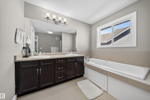 Bathroom featuring a dual vanity with dark wood-finish cabinetry, light-toned countertop, and a large mirror - 3639 15A Street, Edmonton, AB - Indoor Photo Showing Bathroom