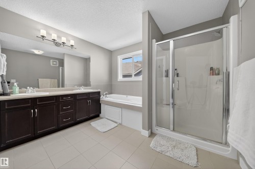 Bathroom featuring a dual vanity with dark wood cabinetry, a built-in bathtub, a glass-enclosed shower, and neutral-toned tile flooring - 3639 15A Street, Edmonton, AB - Indoor Photo Showing Bathroom