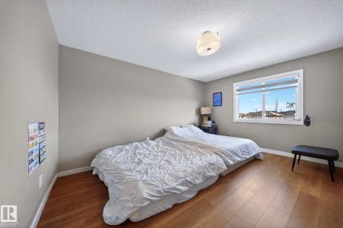 Spacious room featuring wood-finish flooring, a large window with white trim, and a ceiling-mounted light fixture - 3639 15A Street, Edmonton, AB - Indoor Photo Showing Bedroom
