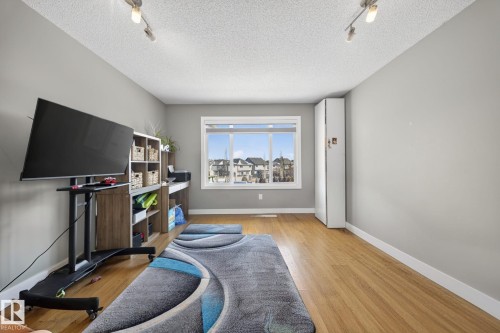 Room with light gray walls and wood-finish flooring, featuring a large window with white trim, track lighting, and a built-in white storage cabinet - 3639 15A Street, Edmonton, AB - Indoor