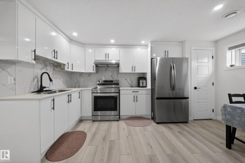 Contemporary kitchen featuring white gloss cabinetry with matte black hardware, light-toned countertops, and a white marble-patterned backsplash - 3639 15A Street, Edmonton, AB - Indoor Photo Showing Kitchen With Upgraded Kitchen