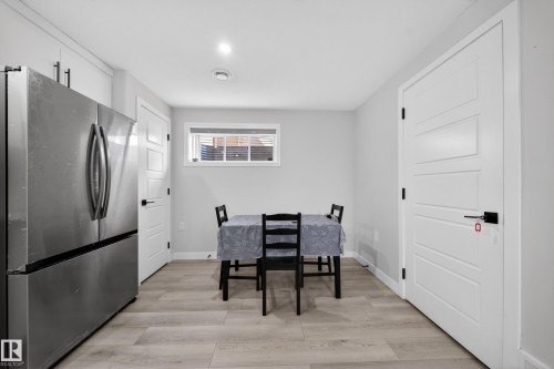 Stainless steel refrigerator with a bottom freezer, light wood-finish flooring, white paneled doors with matte black hardware, recessed lighting, and a horizontal window with blinds - 3639 15A Street, Edmonton, AB - Indoor