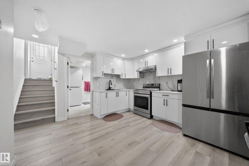 Contemporary kitchen featuring light wood-finish flooring, white cabinetry with dark hardware, stainless steel appliances, and a tiled backsplash - 3639 15A Street, Edmonton, AB - Indoor Photo Showing Kitchen