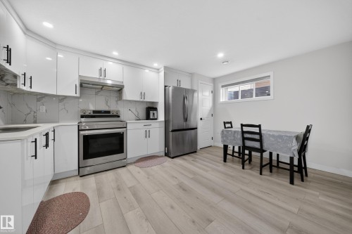 Contemporary kitchen featuring white cabinetry, stainless steel appliances, light-toned wood-finish flooring, and a window for natural light - 3639 15A Street, Edmonton, AB - Indoor Photo Showing Kitchen