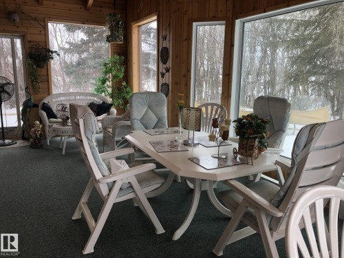 Enclosed sunroom featuring wood paneling, extensive window-line, and plush green carpeting - 123064 Hwy 45, Rural Two Hills County, AB 