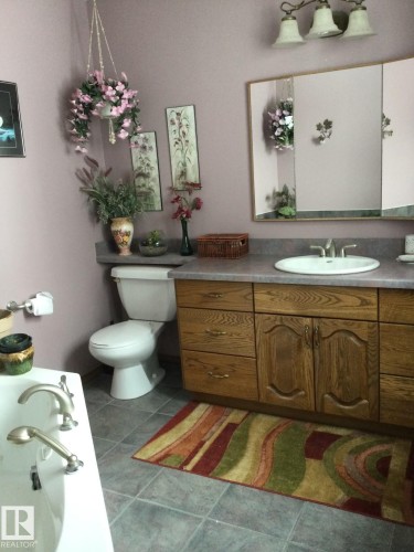 Bathroom featuring a light-colored vanity with a built-in sink, a wall-mounted mirror, and a three-light fixture overhead - 123064 Hwy 45, Rural Two Hills County, AB 