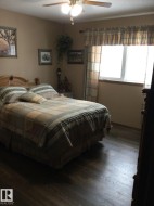Spacious room featuring wood-finish flooring, a ceiling fan with integrated lighting, and a window with wood trim - 