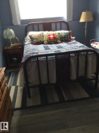 Wood-finish flooring with a striped area rug, complemented by a metal frame bed and a window with white blinds - 
