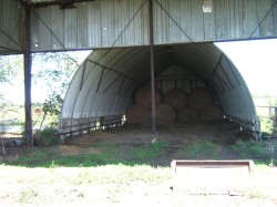 Quonset hut-style barn with a corrugated metal roof and a partial wood fence base - 