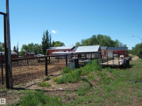 Agricultural property featuring multiple red outbuildings with metal roofs, fenced corrals, and established perimeter trees - 123064 Hwy 45, Rural Two Hills County, AB 