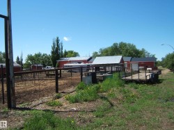 Agricultural property featuring multiple red outbuildings with metal roofs, fenced corrals, and established perimeter trees - 