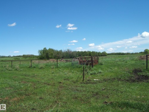 Expansive green pastureland featuring perimeter fencing, an enclosed feeding area, and a distant tree line defining the property's edge - 123064 Hwy 45, Rural Two Hills County, AB 