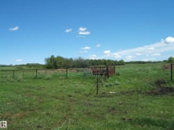 Expansive green pastureland featuring perimeter fencing, an enclosed feeding area, and a distant tree line defining the property's edge - 
