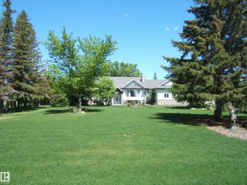 Expansive green lawn with mature evergreen and deciduous trees framing a traditional-style residence - 123064 Hwy 45, Rural Two Hills County, AB 