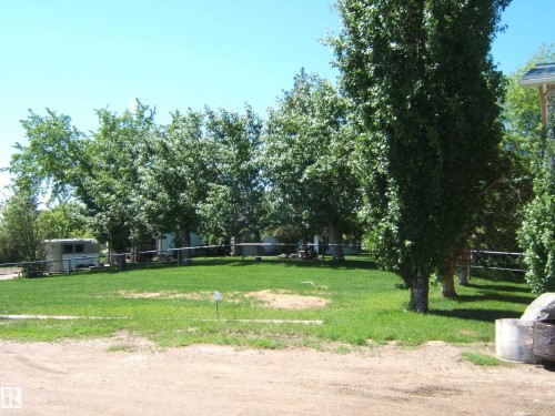 Expansive green lawn surrounded by mature trees, featuring a light-colored utility building, a gray-toned outdoor structure, and a perimeter fence - 123064 Hwy 45, Rural Two Hills County, AB 