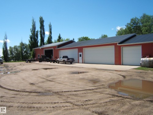 Red industrial building featuring a metal roof, multiple large white garage doors, and a concrete apron - 123064 Hwy 45, Rural Two Hills County, AB 