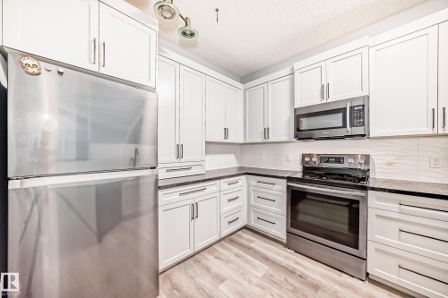 Kitchen with stainless steel appliances, white cabinets, light wood finished floors, a textured ceiling, and dark stone countertops - 507 11716 100 Avenue, Edmonton, AB - Indoor Photo Showing Kitchen