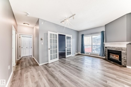Unfurnished living room with french doors, a fireplace, light wood-style flooring, track lighting, and baseboard heating - 507 11716 100 Avenue, Edmonton, AB - Indoor Photo Showing Living Room With Fireplace