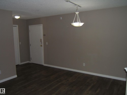 Entry area featuring wood-finish flooring, neutral wall tones, white baseboards, and a contemporary ceiling fixture - 105 11214 80 Street, Edmonton, AB - Indoor Photo Showing Other Room